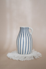 modern striped blue and white vase standing on a white coaster. Minimal boho styled interior design, living room or bedroom decor.