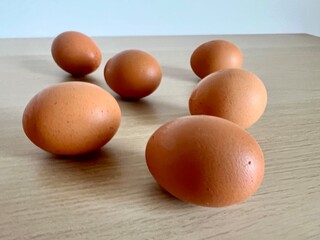 A few brown eggs on a wooden table with a white wall background. Perfect for fresh food themes, healthy eating, protein-rich diets, or Easter designs highlighting simplicity and tradition.