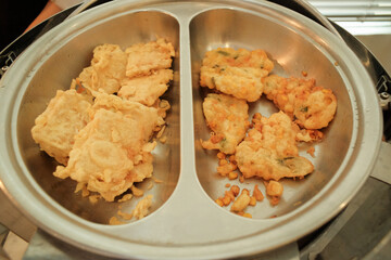 Crispy battered fried tempeh and vegetable fritters (bakwan) served in a stainless steel container, highlighting a popular Indonesian snack