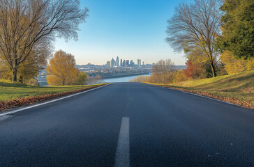 Fototapeta premium A wide road leads to the city skyline, overlooking the river with trees on both sides. The asphalt surface is clean and smooth, with white lines at its edge