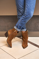 Stylish suede boots, worn with rolled-up jeans, showcasing fringe details and studded accents,...