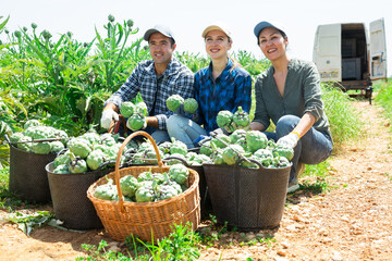 Happy farmers posing with harvest of artichoke on the field