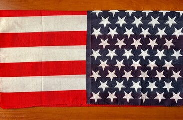 Fototapeta premium Bright, vibrant American flag with red and white stripes and blue field filled with white stars rests on a wooden table, symbolizing patriotism and national pride during festivities