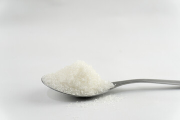 A spoon filled with white sugar, placed on a pristine white surface.