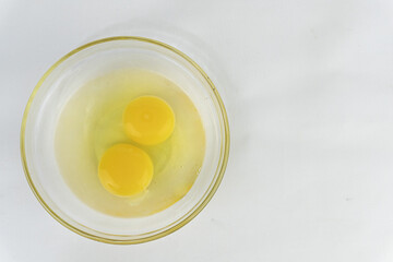 Two raw egg yolks in a glass bowl on a white surface, ideal for food photography and culinary applications.