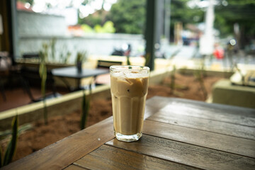 An iced café latte placed on a table with a blurred background of multiple tables in an outdoor setting, creating a relaxed café atmosphere