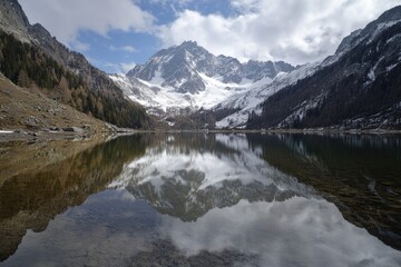 Fototapeta premium Breathtaking alpine scenery featuring a tranquil lake reflecting majestic snow-capped peaks, ideal for nature lovers and photographers.