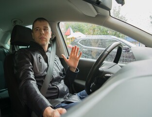A serious driver wearing a seat belt waves to another driver, giving way to him