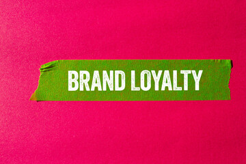 Brand loyalty message written on ripped torn green paper tape on pink background. Conceptual brand loyalty symbol. Copy space.