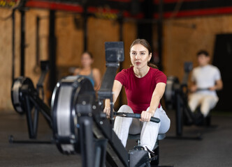 Woman exercises on a rowing machine in the gym. European is preparing for the rowing competition....