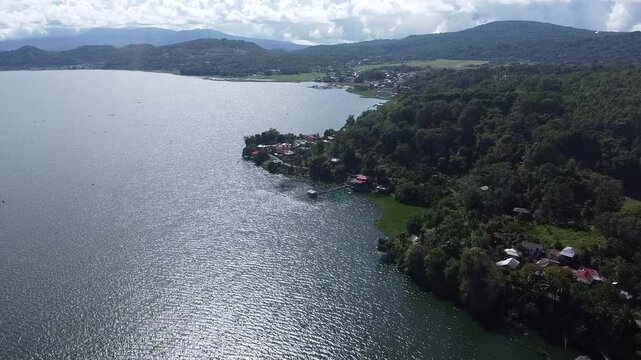 Aerial drone footage of Lake Tondano, North Sulawesi, Indonesia, showcasing calm waters, lush green hills, and lakeside settlements under a bright sky