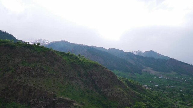 Landscape shot of green Himalayas during the summer season surrounded by dark stormy clouds as seen near Triloknath village in Pattan Valley of Lahaul and Spiti district, Himachal Pradesh, India.