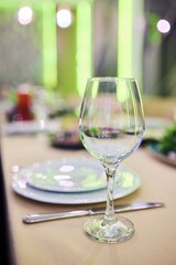 A wine glass sits on a table with a white plate and silverware. The table setting is elegant and sophisticated, with a focus on the wine glass as the centerpiece.