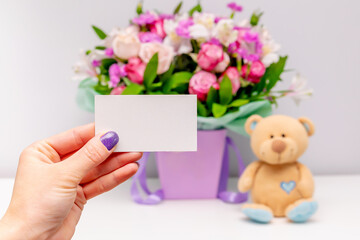 Obraz premium Female hand with cutout,blank business card on flowers bouquet background.florist shop mockup design template.Womens,Valentines,Mother day gift.