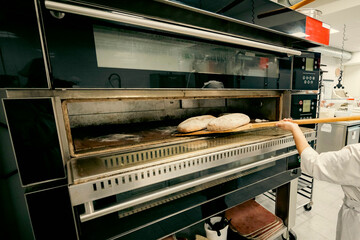 Freshly baked bread being removed from a modern professional oven in a bakery. Artisan baking process in a commercial kitchen with high-tech equipment.