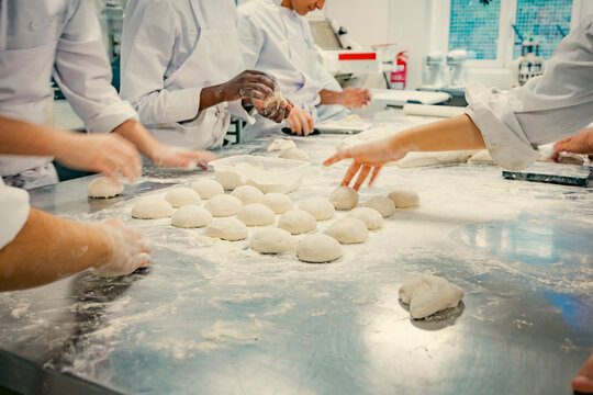 Hands of baking students working with fresh dough in a professional kitchen. Artisan bread preparation, teamwork, and pastry training in a culinary school. Flour, dough balls, and rolling techniques.