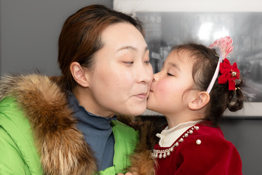 A little girl in a red formal dress with bows in her hair celebrates her birthday, kissing her mother because she is looking forward to a birthday cake with candles and lots of gifts and good wishes