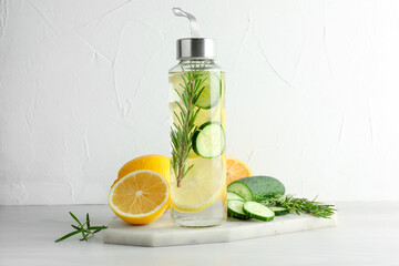 Lemon water in bottle, rosemary, fresh fruits and cucumber on light table