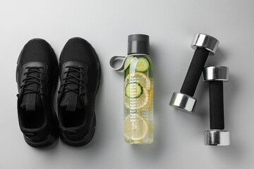 Lemon water in bottle, sneakers and dumbbells on white background, flat lay