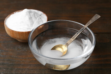 Bowl with water and baking soda on wooden table, closeup