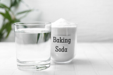Glass of water and baking soda on white tiled table