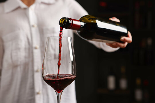Professional sommelier pouring red wine into glass indoors, closeup