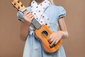 Little girl with ukulele on brown background, closeup