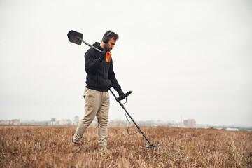 Holding a shovel. Man is with metal detector in the field