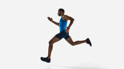 Side low angle view of muscular man, runner in motion, sprinting, training isolated on white studio background. Concept of sport, competition, endurance, athletics. Copy space