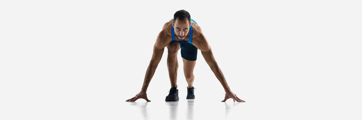 Focused and determined man, runner standing at starting line, ready to run and win isolated on white studio background. Concept of sport, competition, endurance, athletics, sportive lifestyle.