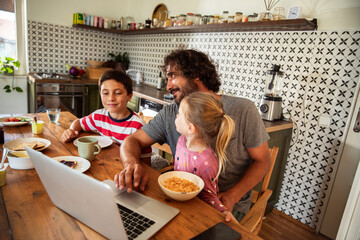 Father with children having breakfast using laptop in kitchen