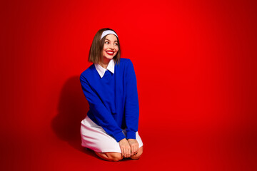 Fototapeta premium Cheerful young woman wearing a blue sweater and a stylish outfit on a vibrant red background