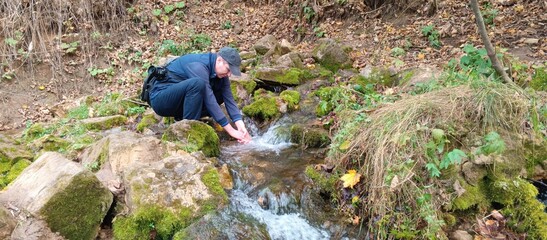 A man with a camera washes his hands in a stream near a spring on an autumn day