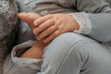 Newborn baby in gray clothes holding own leg with hand