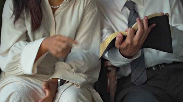 businessman open the book of the bible and read it to a young asian woman father teach his daughter	
