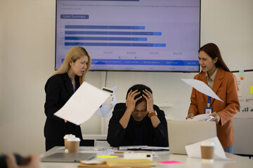 Three people are in a meeting room, with one of them pointing at a laptop screen. The man on the laptop is looking down, and the other two people are looking at him. Scene is tense and serious
