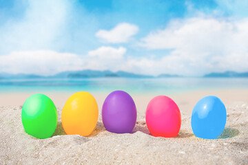 colorful eggs on white sand beach over blue sea, happy Easter or summer holiday concept.