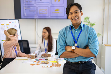 A man in a blue shirt and black pants is smiling and standing in front of a white table. He is...