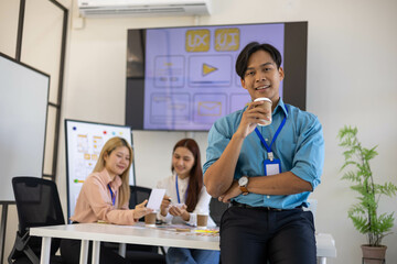 A man in a blue shirt and black pants is smiling and standing in front of a white table. He is wearing a blue lanyard and a watch. Concept of professionalism and confidence

