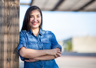 Confident woman smiling in denim while standing with arms crossed outdoors