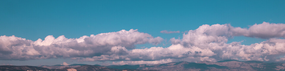 4x1 banner is a band of white cumulus clouds hanging low over the rolling horizon of a blue sky