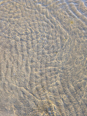 Clear summer sea water with sunlight reflections and visible sand beneath, creating a serene...