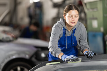 Girl worker removes dents on cars exterior, restores vehicle to its original form. Female auto...