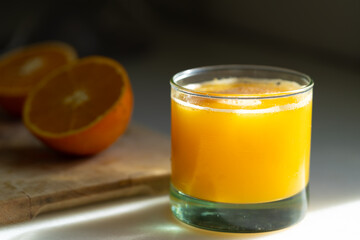 A glass of freshly squeezed orange juice on a kitchen countertop, bathed in warm sunlight, with vibrant orange color and refreshing feel.