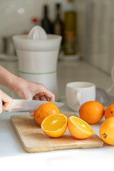 A young woman in a bright kitchen slices fresh oranges on a wooden cutting board, preparing juice. Sunlight streams in, illuminating her hands and the vibrant citrus fruit.