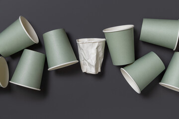 New light green paper cups and crumpled used white one on a dark gray top view, mockup