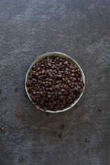 Pile of coffee beans in a bowl spilling over the side on a dark and moody background. Overhead top shot