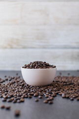 Pile of coffee beans in a bowl spilling over the side on a dark and moody background. Side angle
