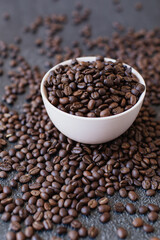 Pile of coffee beans in a bowl spilling over the side on a dark and moody background. 