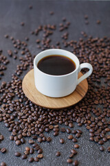 Espresso coffee served in white cup with wooden saucer on dark moody background with roasted coffee beans scattered
